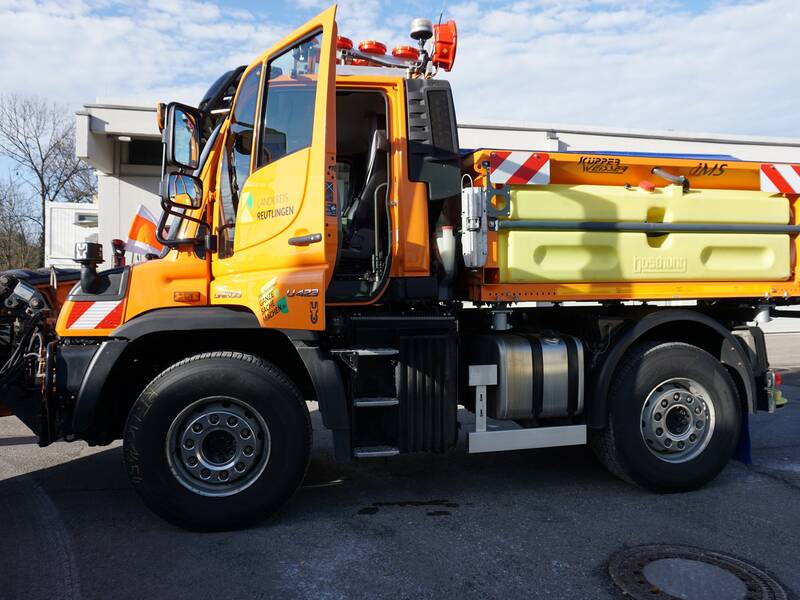 Ein orangefarbenes Spezialfahrzeug mit einer gelben Ladefläche und Aufschriften des Landkreises Reutlingen steht vor einer Gebäudekulisse.