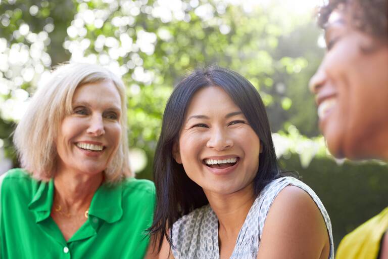 Drei Frauen im Freien lachen zusammen.