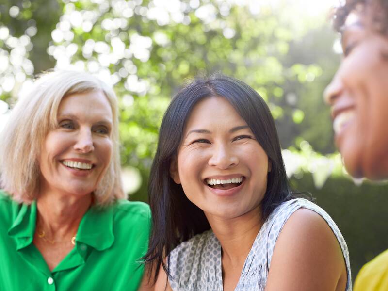 Drei Frauen im Freien lachen zusammen.