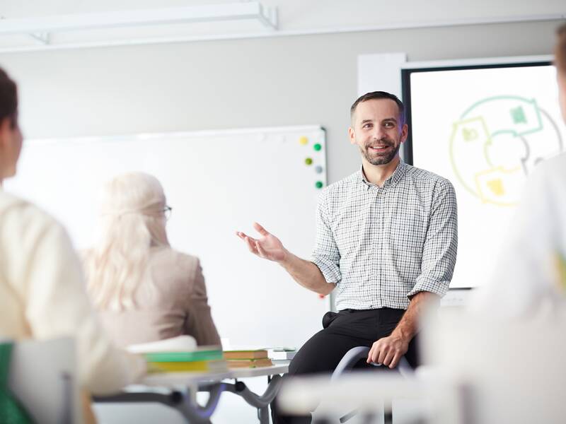 Ein Mann steht vor einem Schulungsraum vor drei Personen. Im Hintergrund ist ein Whiteboard.