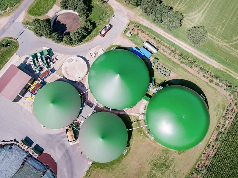 Ein landwirtschaftlicher Betrieb von oben aus der Luft. In der Mitte sind vier runde Gebäude mit grünen Dächern. Rund um die Gebäude sind Felder.