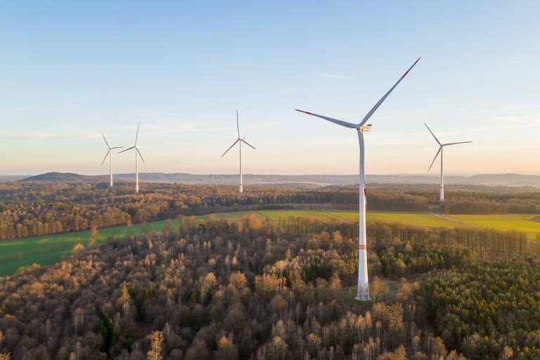 Eine grüne Landschaft mit Bäumen und Wiesen in der fünf Windkrafträder stehen.