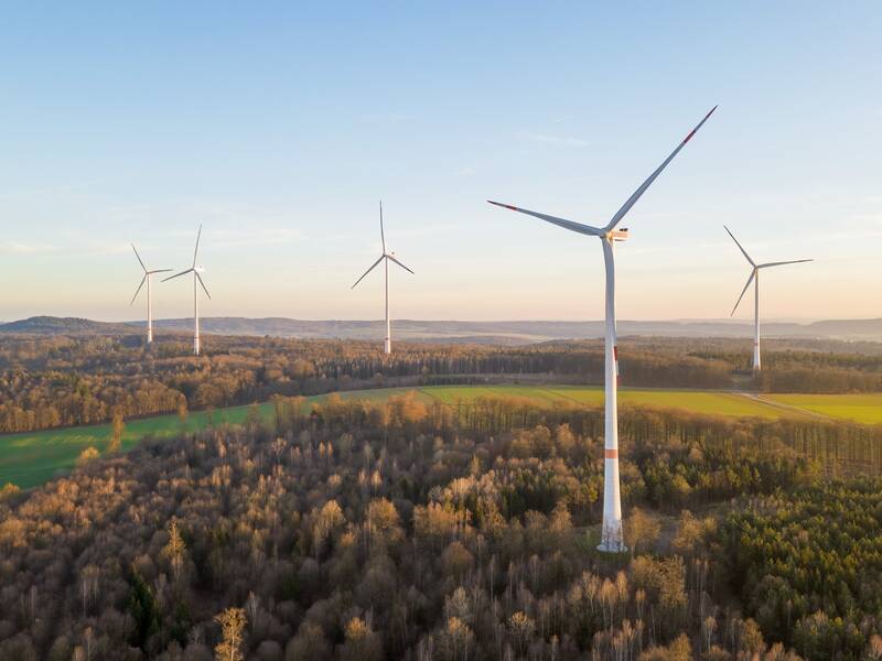 Eine grüne Landschaft mit Bäumen und Wiesen in der fünf Windkrafträder stehen.