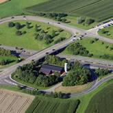 Ein großer Verkehrsknoten mit Straßen und Felder darum herum aus der Luft. Unten rechts ist eine Halle. Dies ist das Streustofflager Walddorfhäslach.