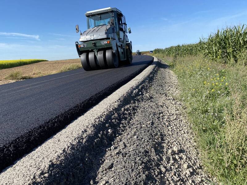 Ein Walzfahrzeug fährt über eine frisch asphaltierte Straße.