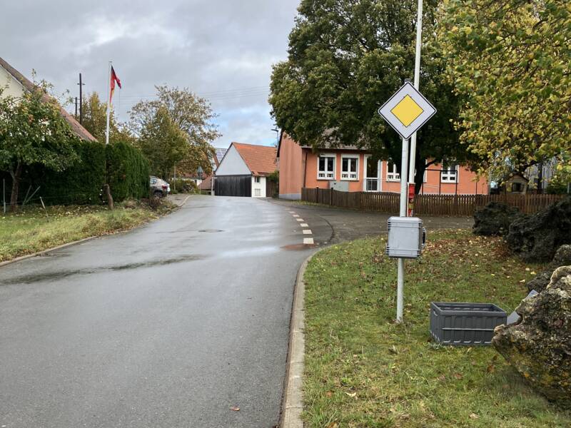 Ein Vorfahrt-Schild steht rechts an einer nassen Straße in einem Wohngebiet.