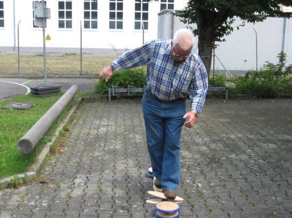 Älterer Herr mit grauen Haaren, Hemd und Jeans balanciert auf Platten.