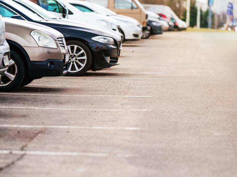 Bilck auf grauen Parkplatz mit einer Reihe parkender Autos am linken Bildrand