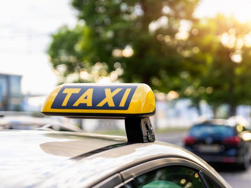 Dach eines gelben Taxis mit Taxischild im Vordergrund parkt an einem Straßenrand