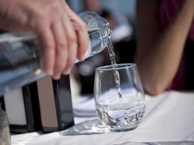 Ein halbgefülltes Glas steht auf einem Tisch mit weißer Tischdecke. Es wird Wasser ins Glas gefüllt