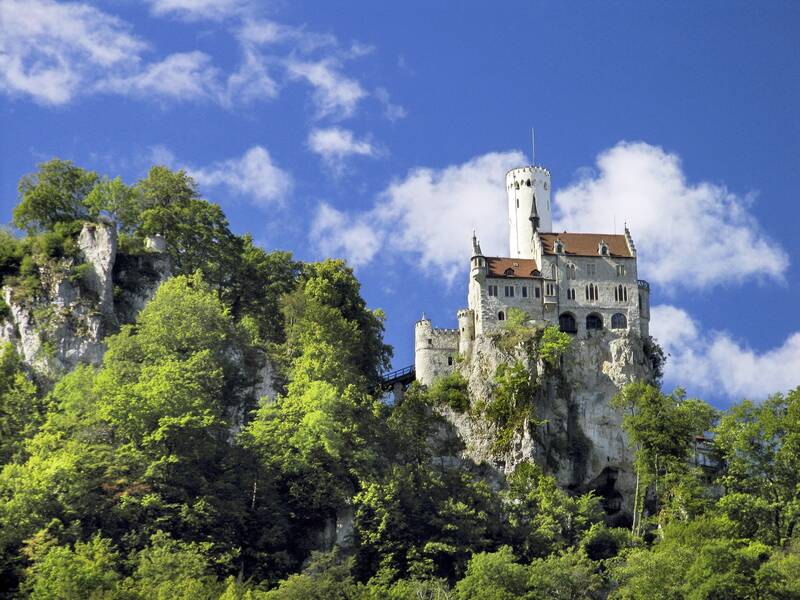 Eine Burg auf einem Berg vor einem leicht bewölktem Himmel. Rund um die Burg sind Bäume.