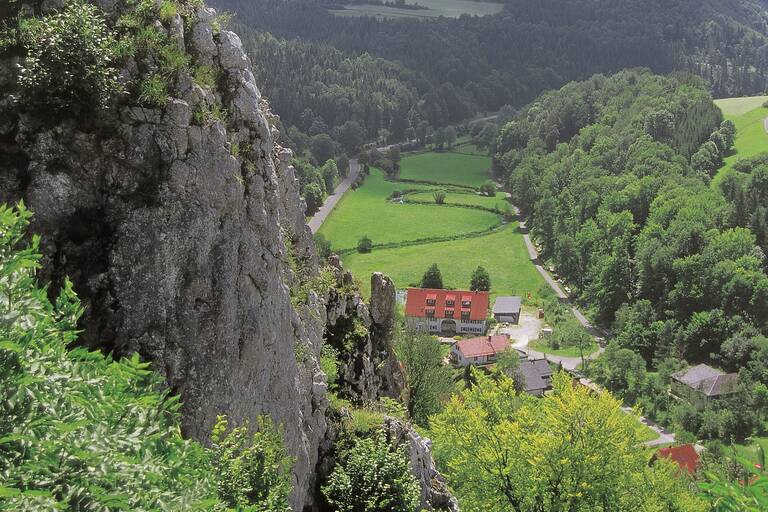 Ein kleines Schlösschen in einem Tal. Rund herum sind Hügel.