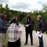 Eine Gruppe mit fünf Personen steht an einem Feldweg. Rechts davon sind Sträucher.