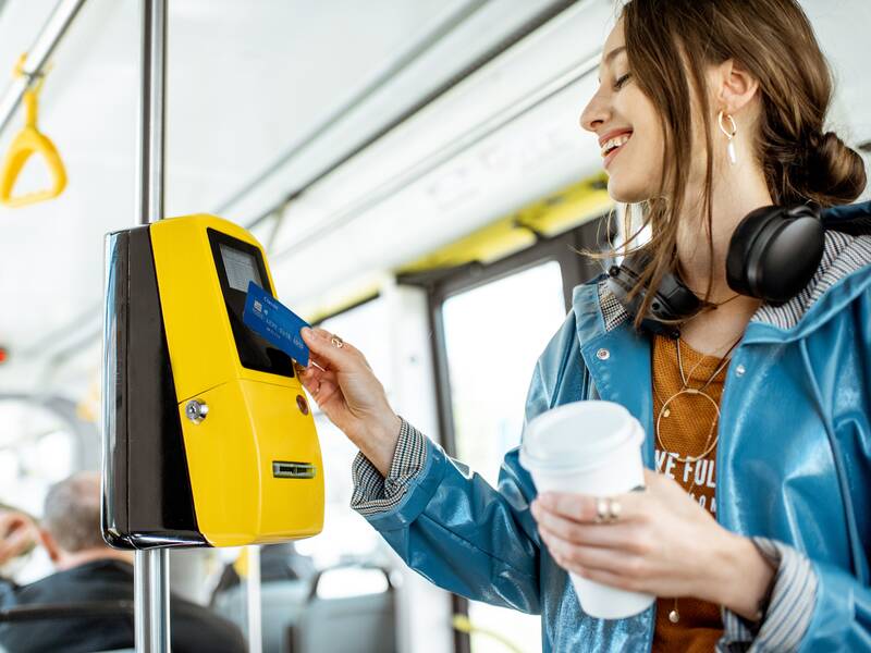 Eine junge Frau kauft in einem Bus eine Fahrkarte an einem Automat.