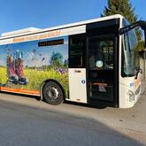 Ein Bus hält auf einer Straße. Auf dem Bus ist ein Bild von Wanderschuhen auf einer Wiese abgebildet.