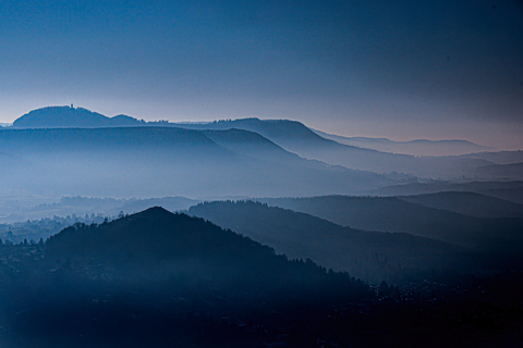 Die Silhouetten mehrerer Berge erscheinen in verschiedenen Blautönen vor einem nebligen Horizont.